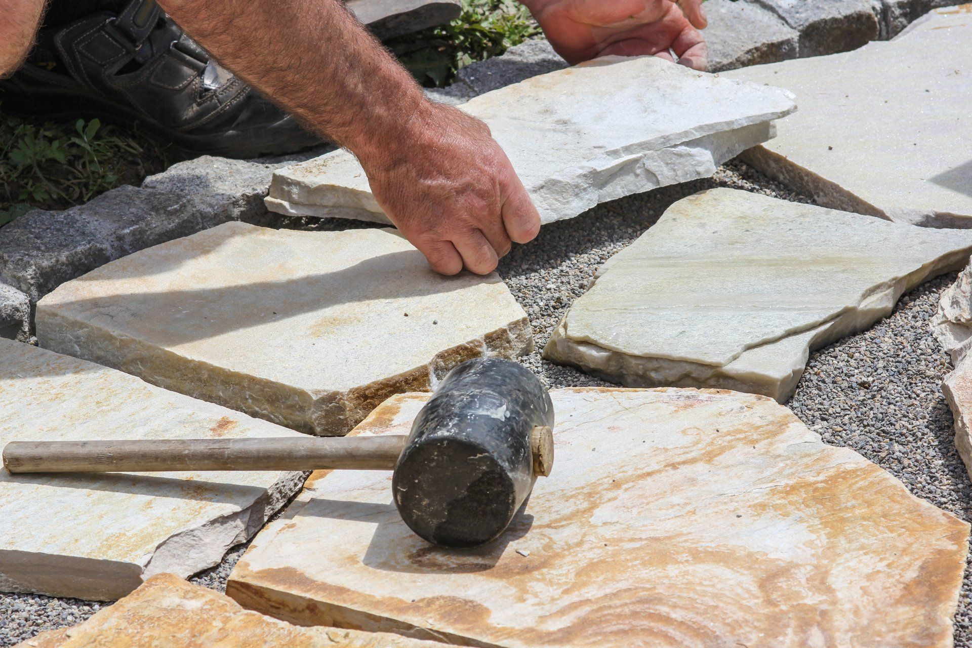 A man is laying rocks on the ground with a hammer.