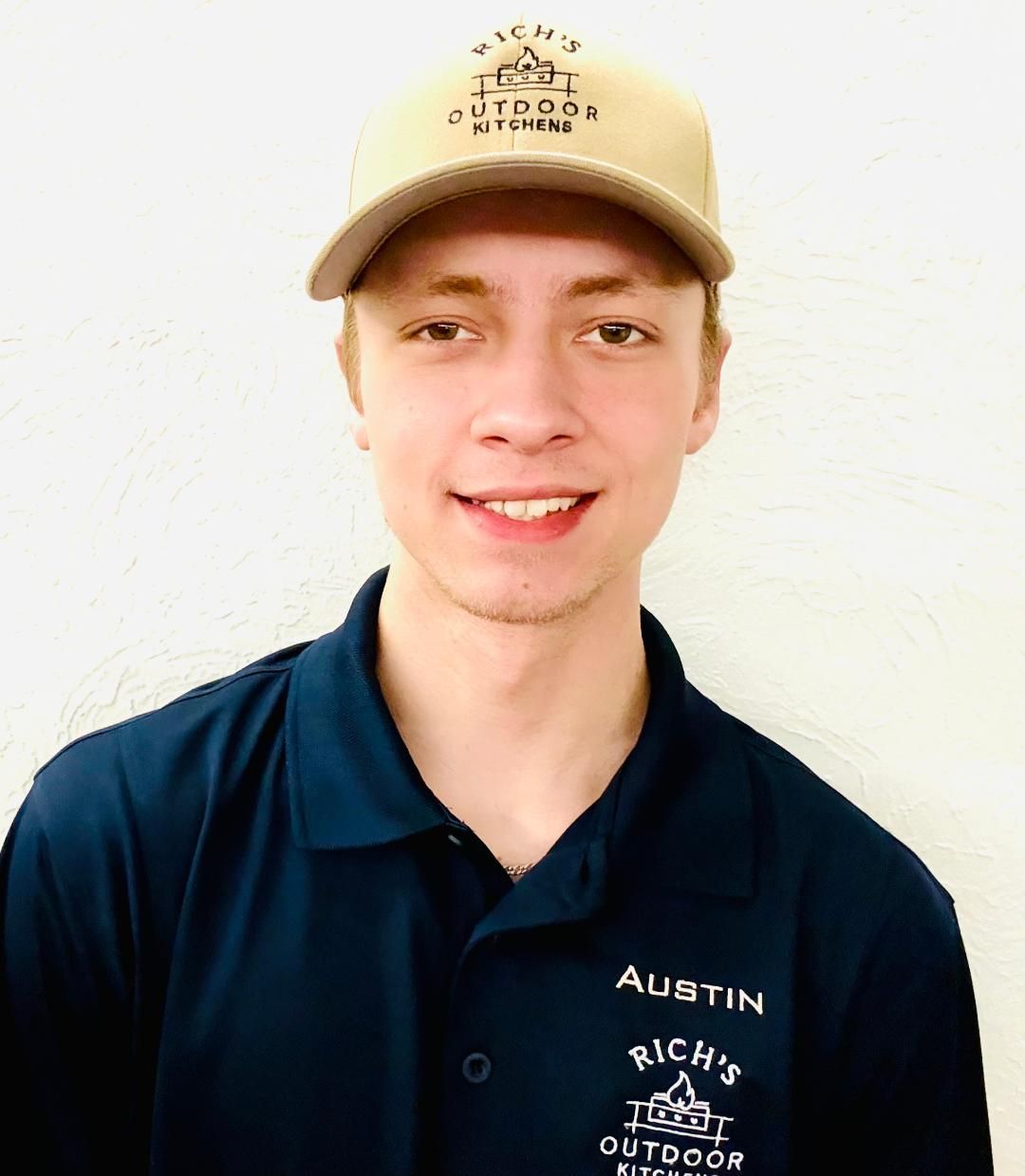 Man wearing tan cap and blue polo shirt, smiling. Name tag says