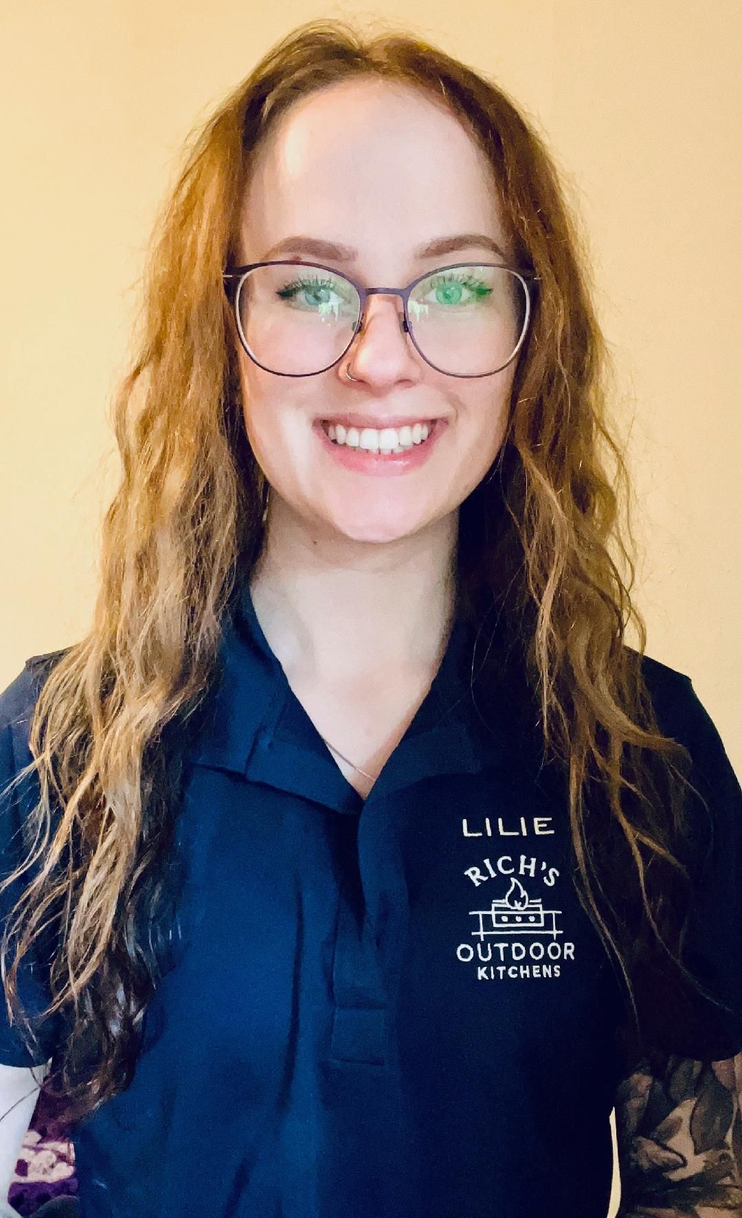 Woman wearing glasses smiles at the camera, wearing a dark blue polo shirt with a logo.