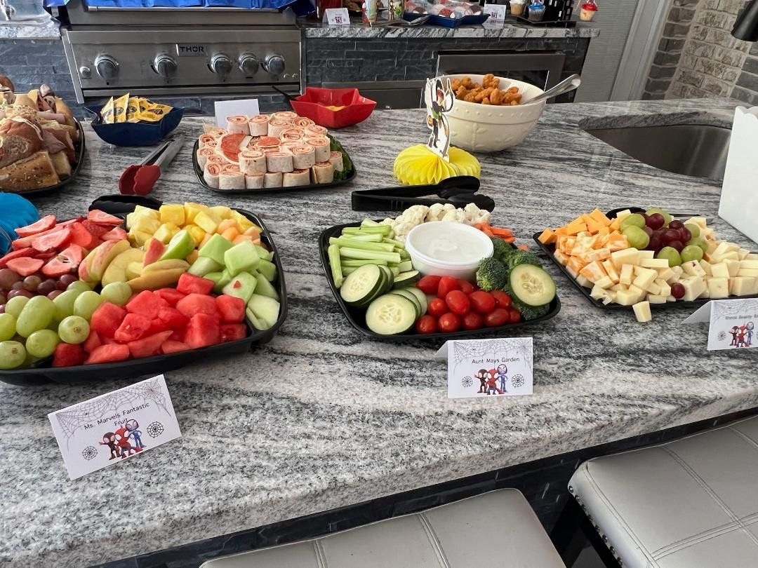 A spread of food platters, including fruit, veggies, cheese, and appetizers, on a countertop, ready for guests.