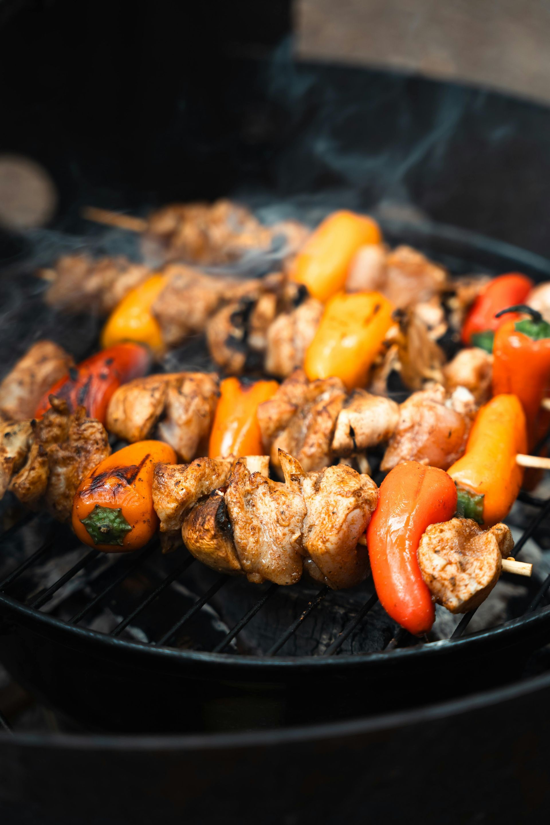 Kabobs of chicken and bell peppers grilling on a charcoal grill.