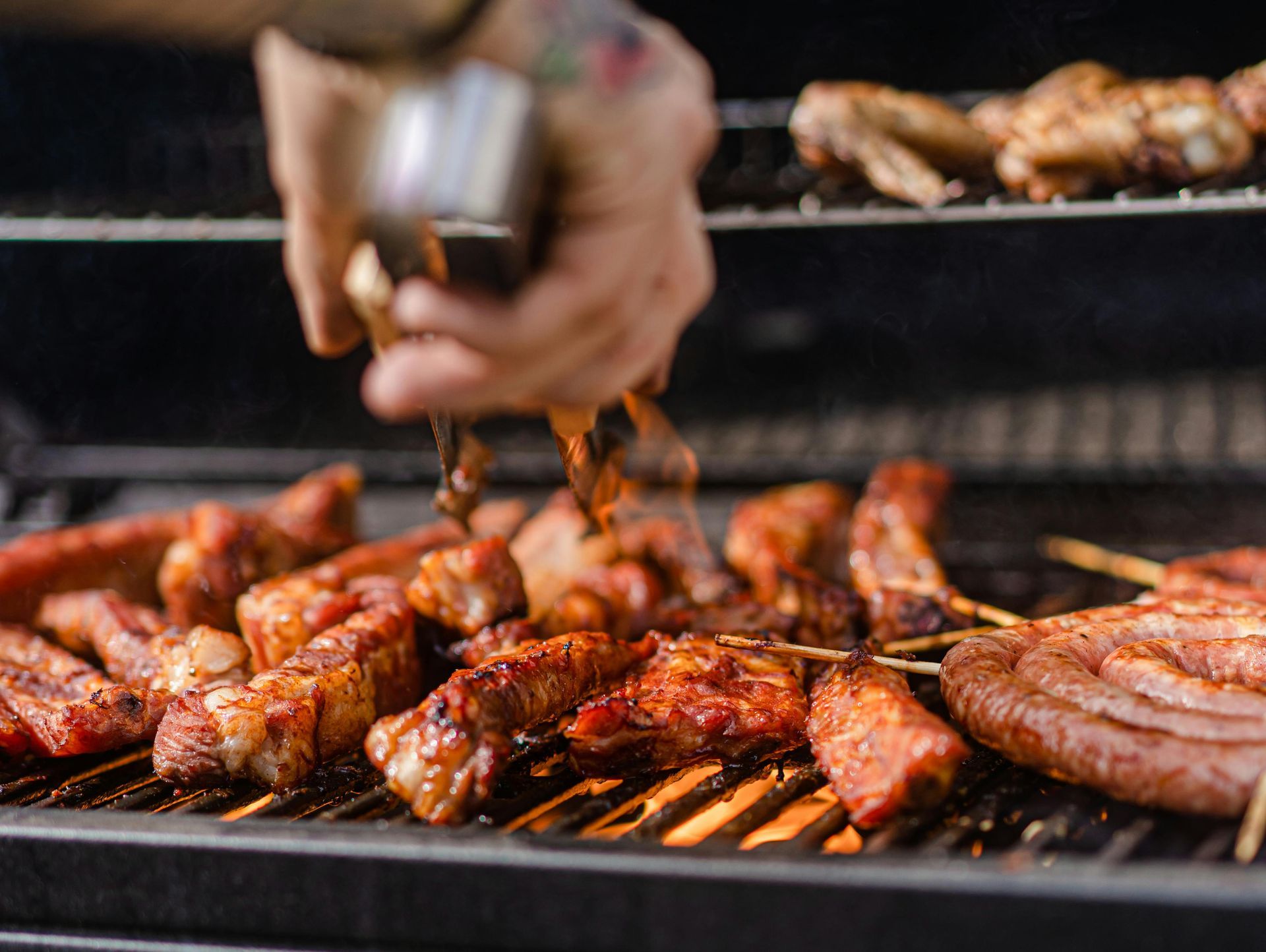 Grilling various meats on a barbecue. A person using tongs flips a piece of meat.