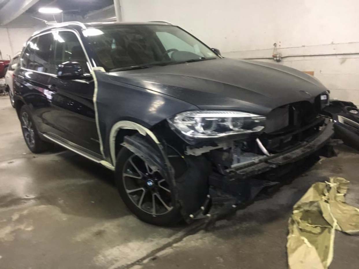 Damaged dark SUV with front-end collision damage in an indoor garage.
