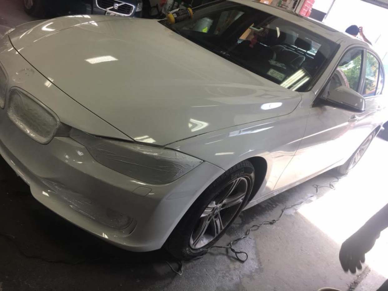 White sports coupe in a garage with its front bumper removed and a wheel exposed