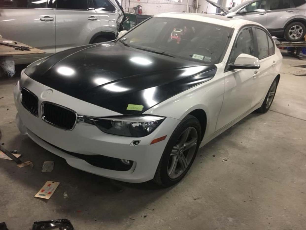 White sports coupe with black hood parked in a garage, front-left view
