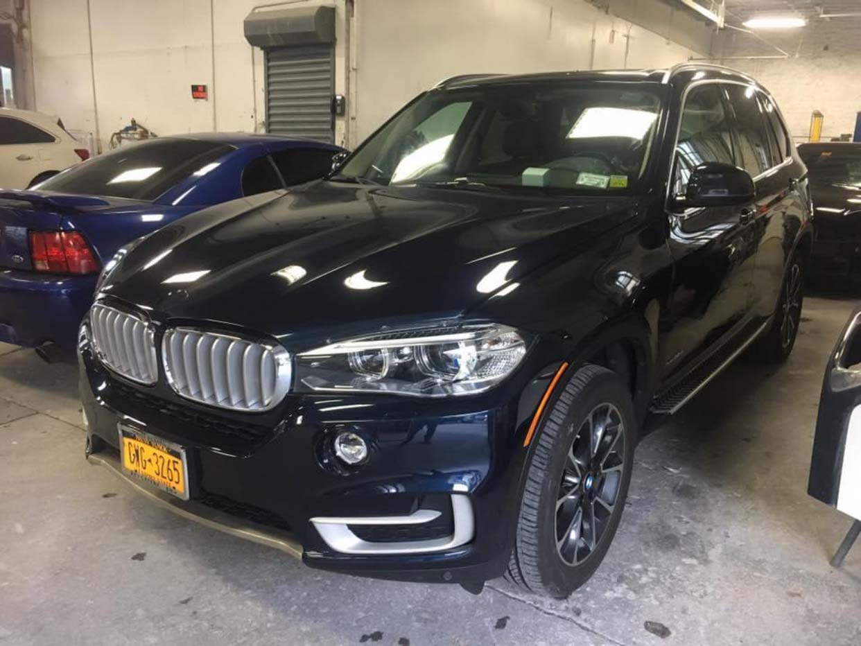 Black BMW SUV parked indoors next to a blue car in a garage or workshop