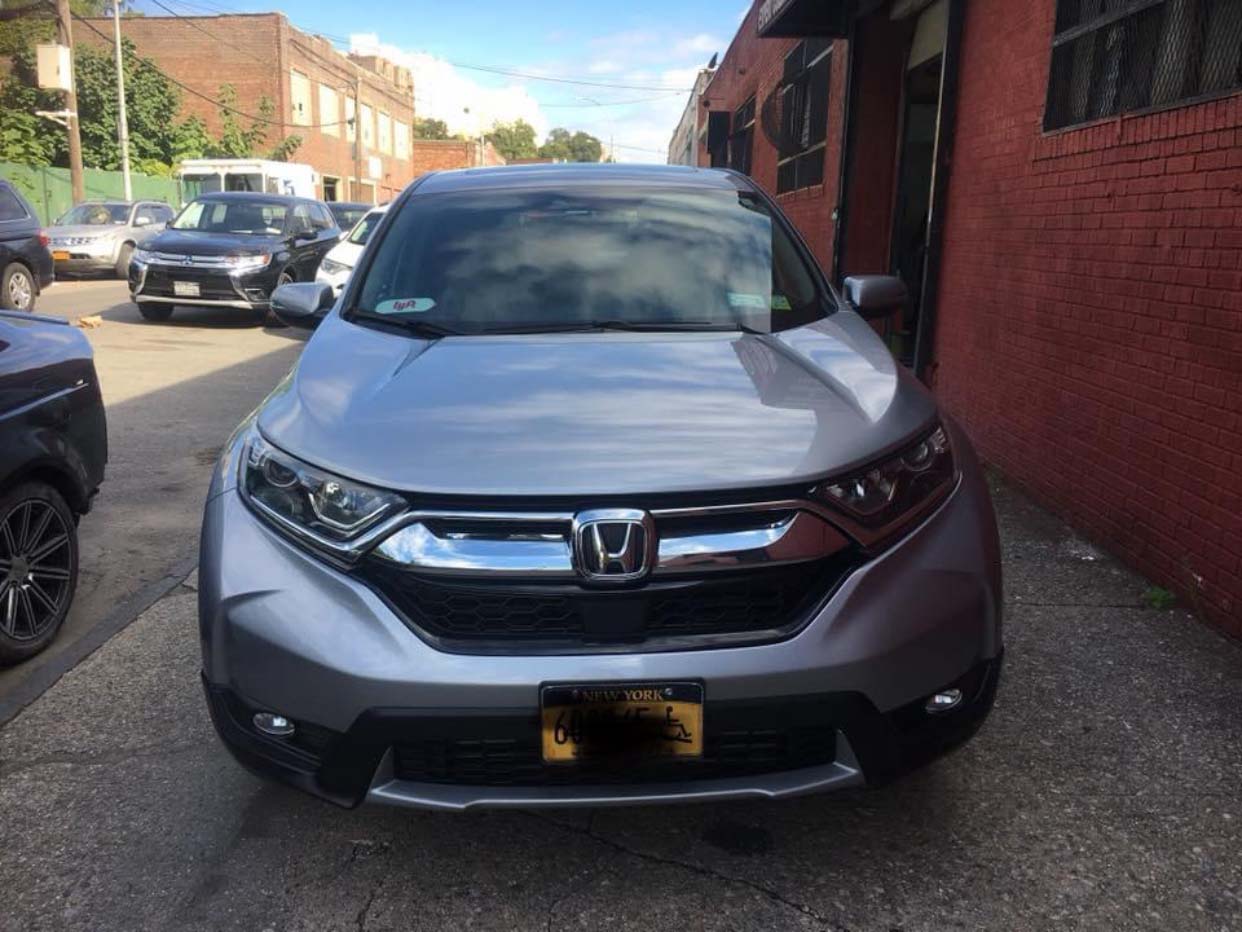 Silver Honda SUV parked on a narrow street beside a red brick building.