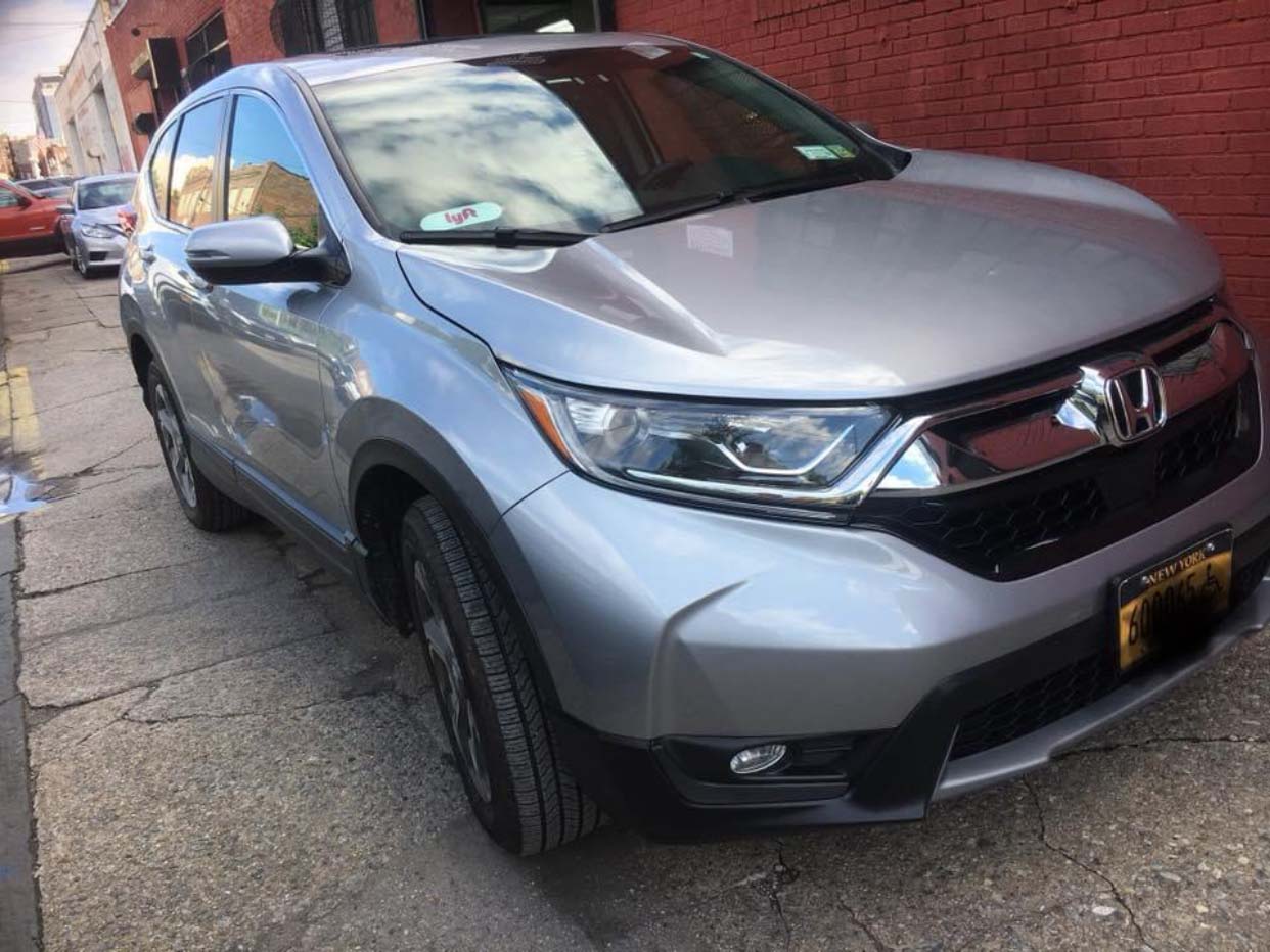 Gray Honda SUV parked on a street beside a brick wall, front-left view.