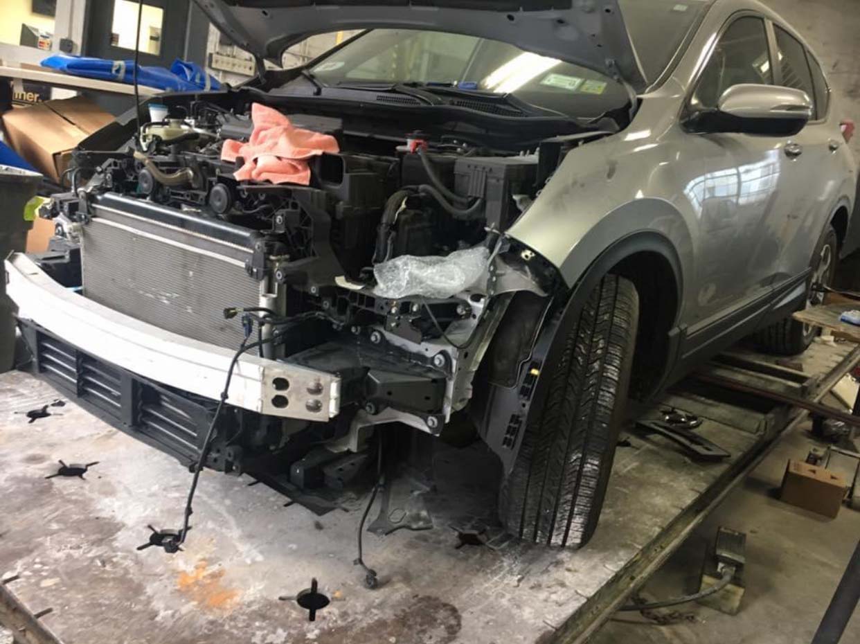 Damaged silver SUV with front-end collision damage in a repair garage, hood open and bumper removed