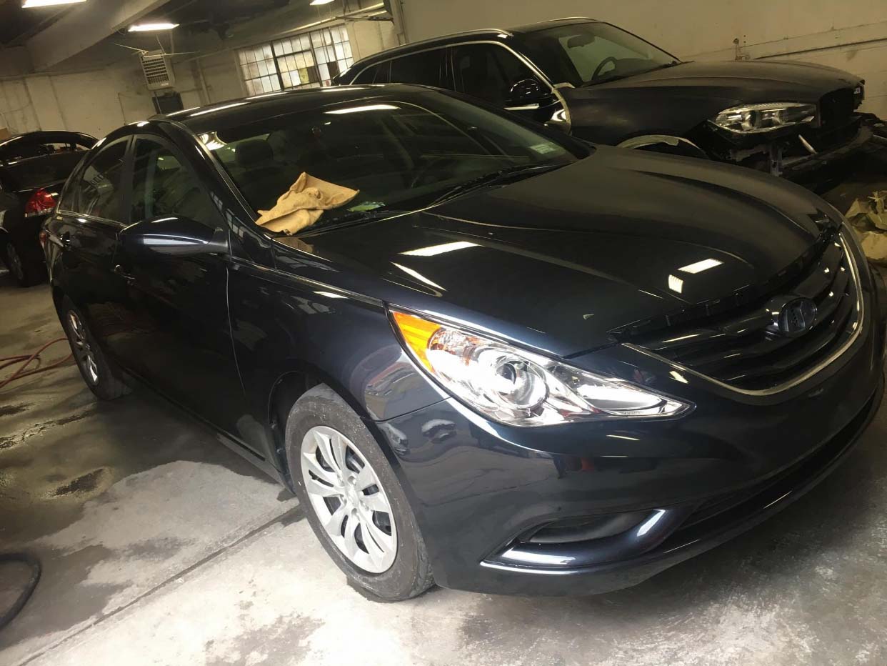Dark blue sedan in a garage with another car parked behind it
