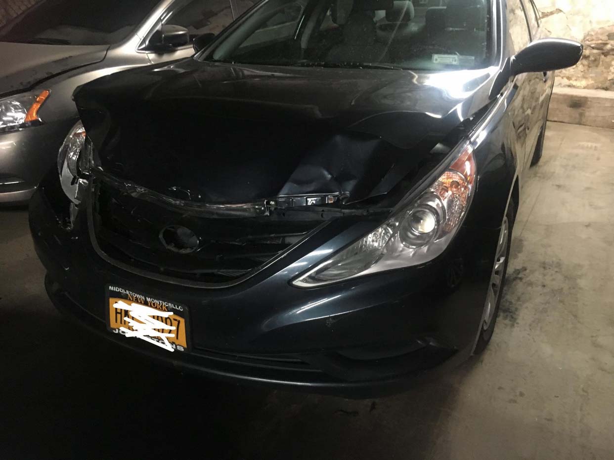 Black sedan parked in a garage with a damaged front hood and grille