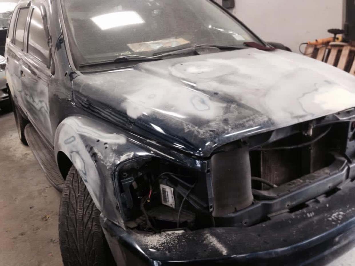 Black SUV with severe front-end damage and white foam residue in a garage
