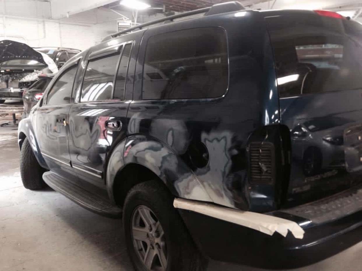 Black SUV with rear-side body damage and primer patches in a parking garage