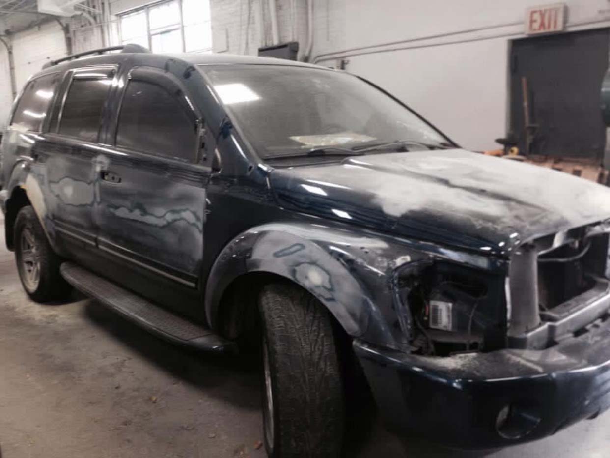 Dark blue SUV with damaged front end in a garage