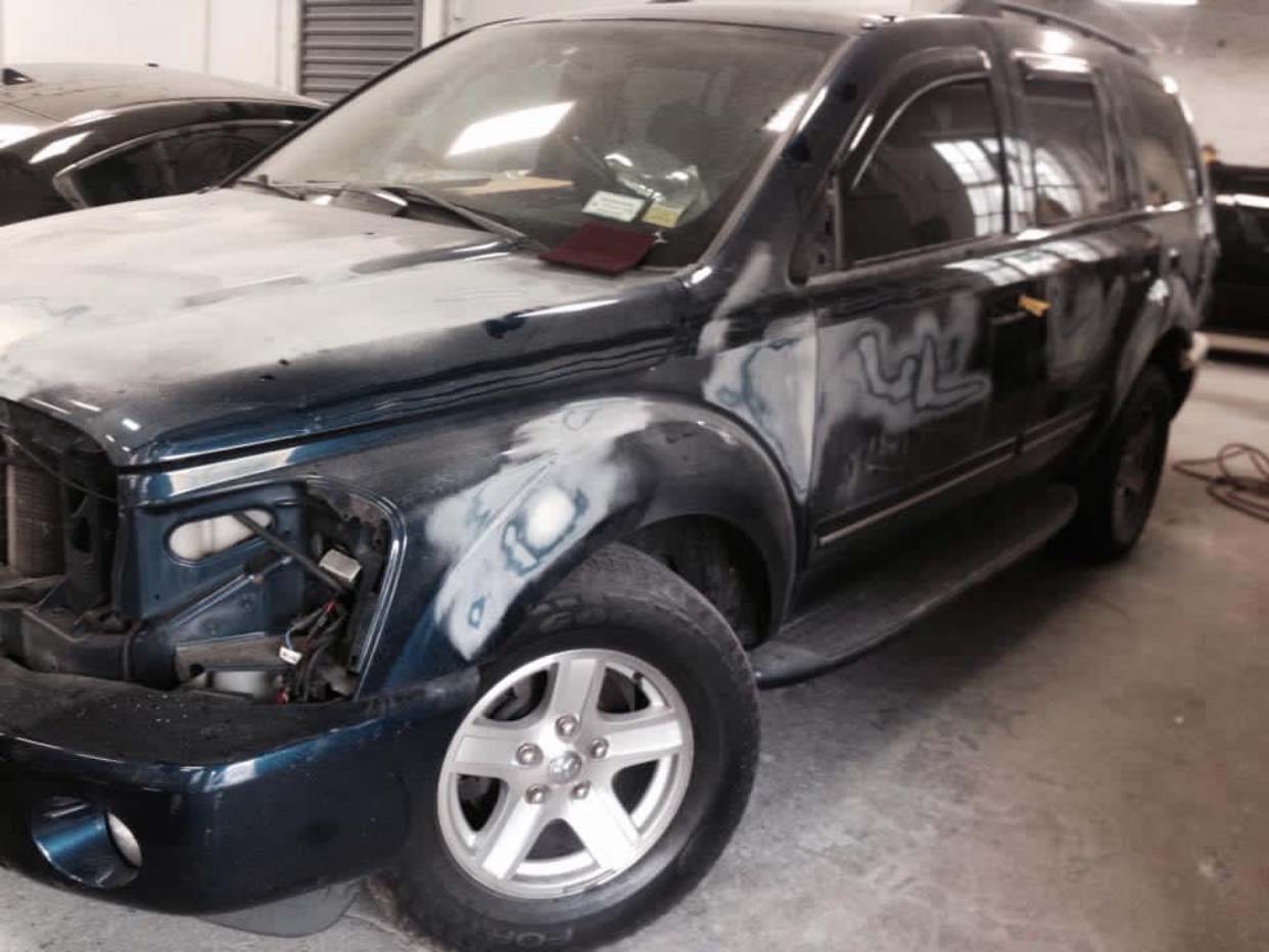 Dark SUV with damaged front end and missing headlight in an indoor garage