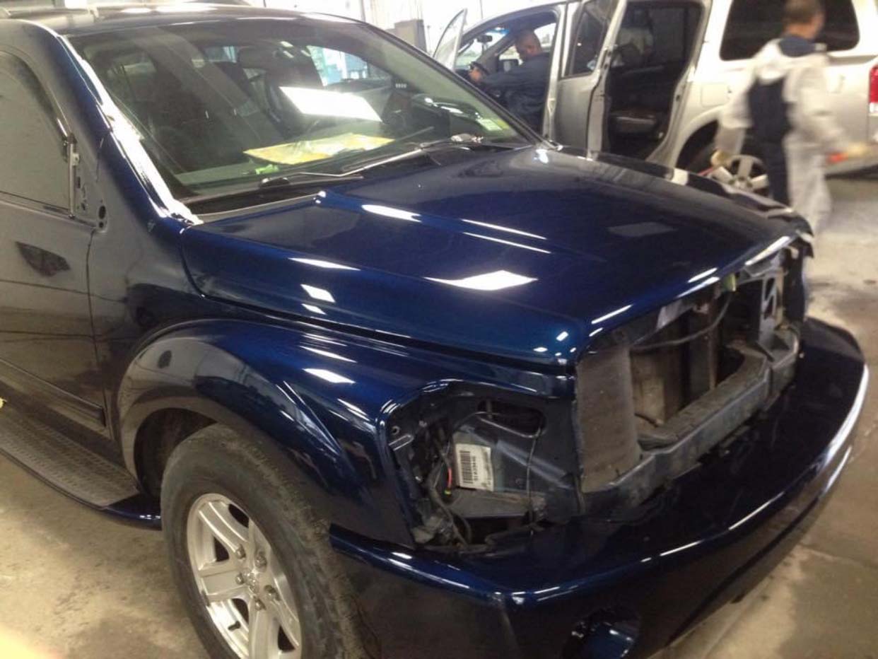 Dark blue SUV with front-end damage, missing headlight, in an indoor garage