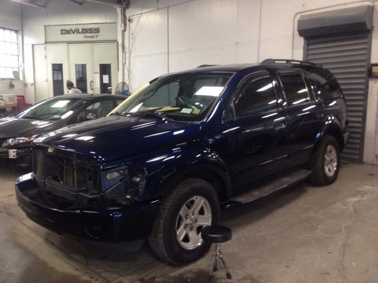 Dark blue SUV in an auto shop bay with a wheel removed and a jack stand underneath.