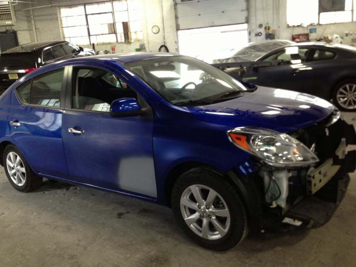 Blue sedan with front-end damage in a garage, parked beside another car