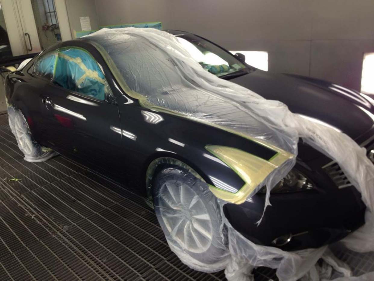 Black sports car in a garage, partially covered in plastic masking for paint or bodywork.
