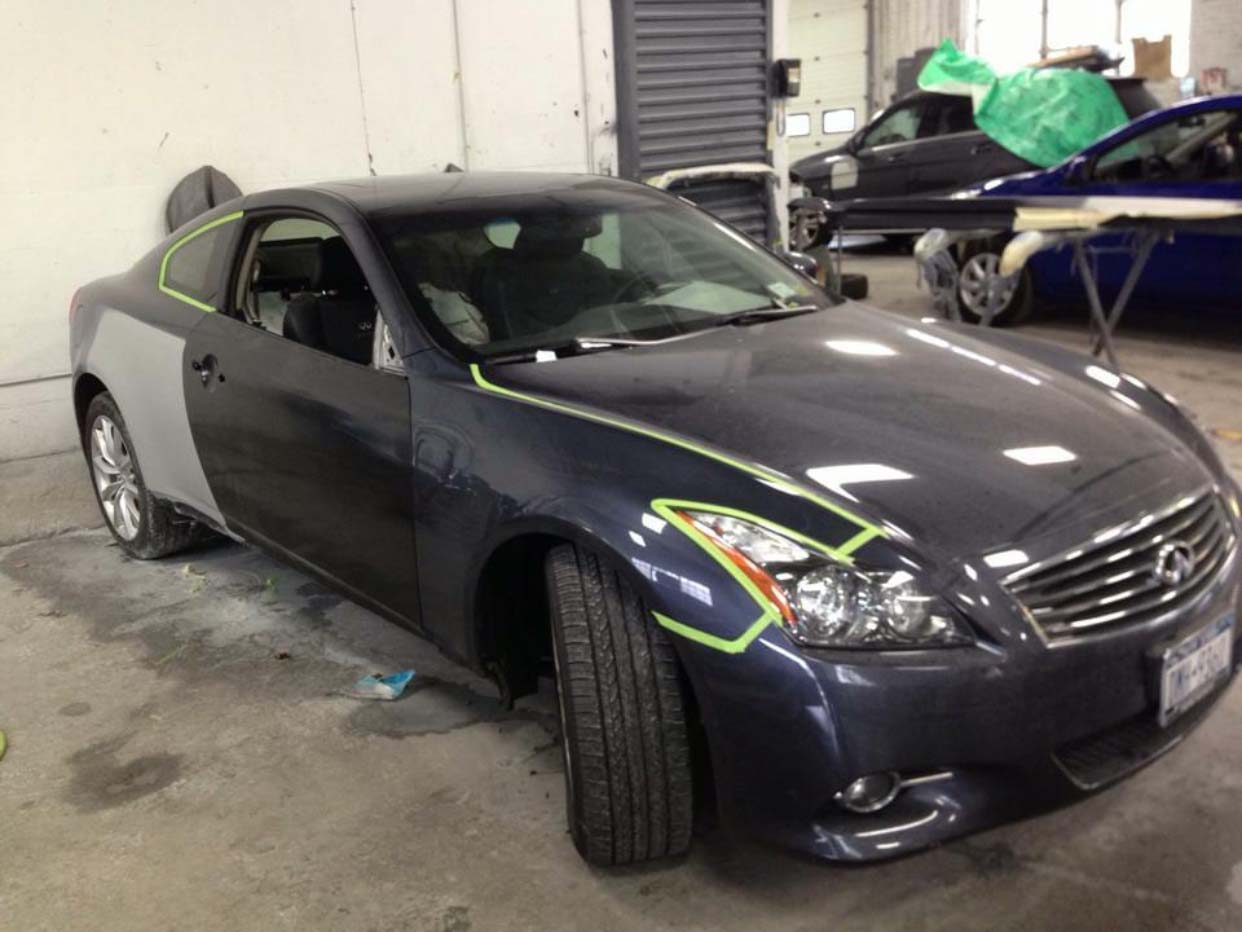 Dark sedan in a garage with a damaged front fender and taped headlight area