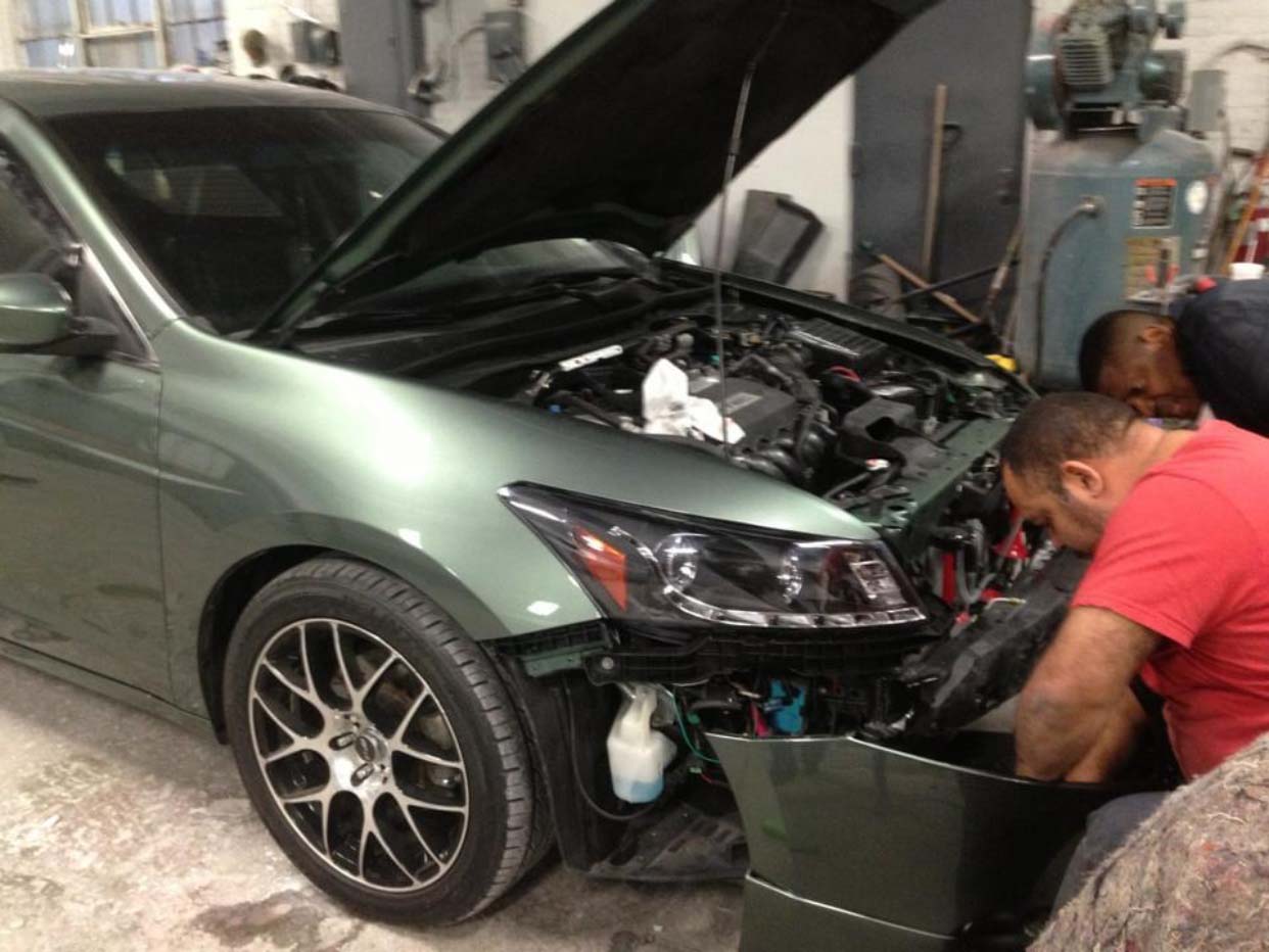Green car with hood open while two mechanics work on the front end in a garage
