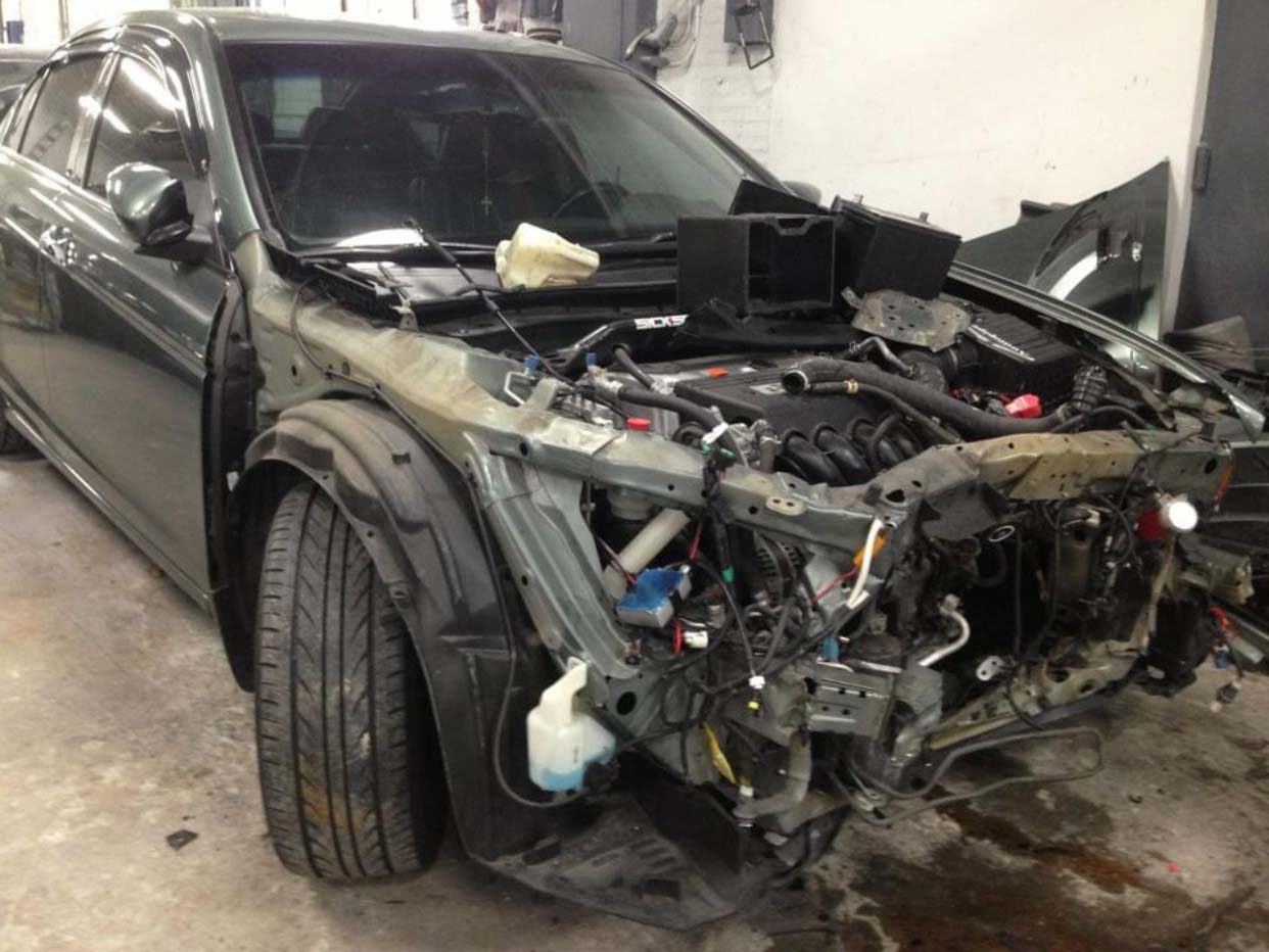 Severely damaged black car in a garage, front end missing and engine exposed