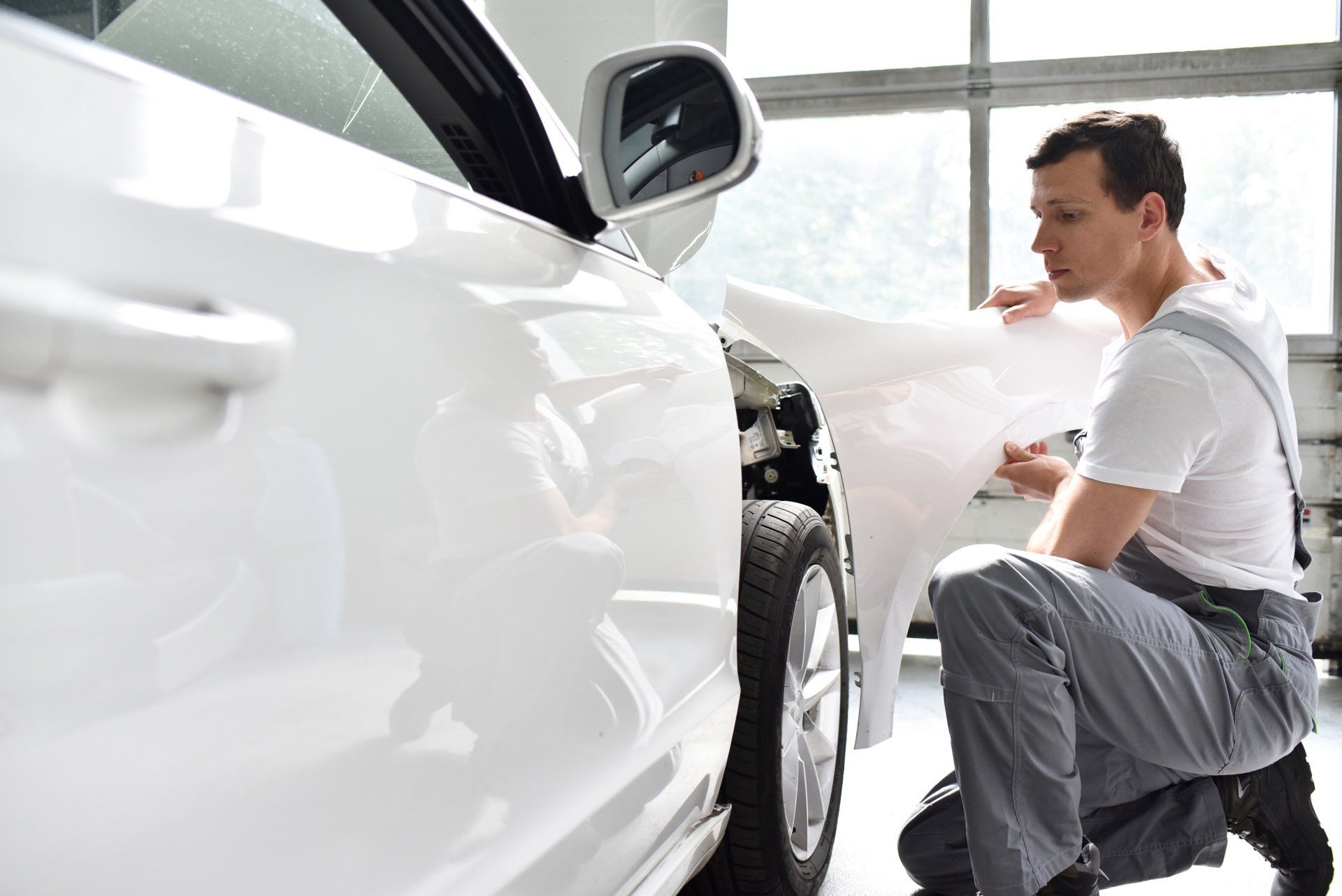 Man inspecting the front wheel of a white car in a bright garage