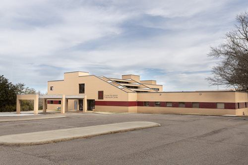 Modern tan building with red stripe and entrance, seen from across an empty parking lot