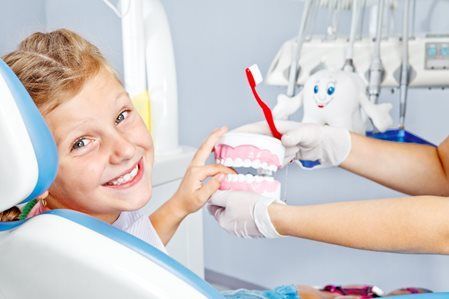 Child smiling in a dentist chair as a dental model is used to show teeth brushing