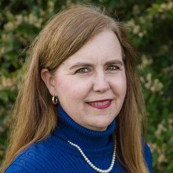 Portrait of a smiling woman in a blue turtleneck and pearl necklace outdoors