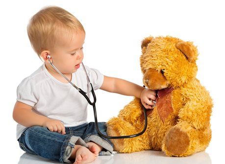 Toddler using a stethoscope to examine a teddy bear on a white background