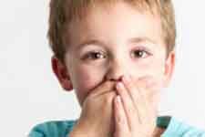Child covering mouth with hands, looking at the camera against a white background.