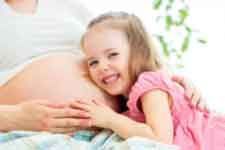 Smiling child hugging a pregnant belly in a bright, white room