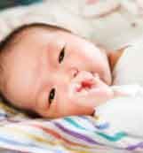 Sleeping baby lying on a colorful blanket, hand near mouth.