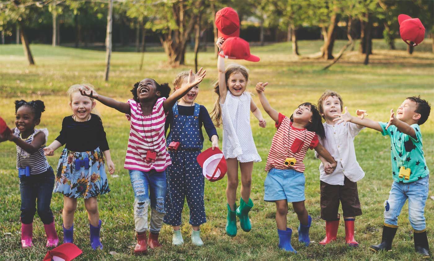 Children in colorful clothes jumping in a grassy park while holding red balloons