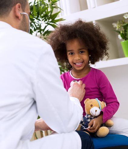 Doctor talking with smiling child holding a teddy bear in a bright office