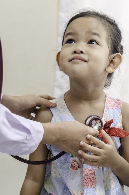 Child being examined with a stethoscope by a clinician, looking up attentively.