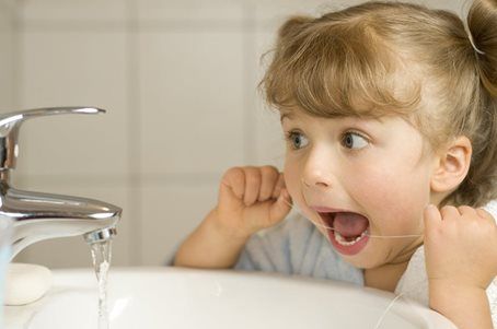 Child brushing teeth at a bathroom sink, looking excited with water running from the faucet