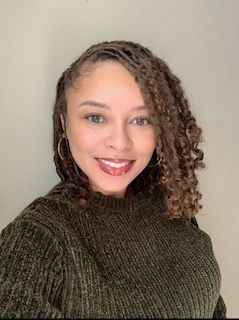 Smiling person in a dark green sweater against a light background