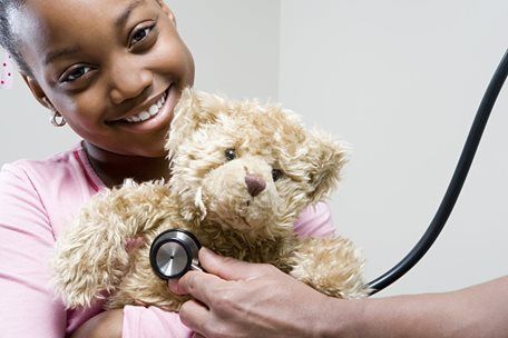 Smiling child holds teddy bear while a doctor uses a stethoscope on it