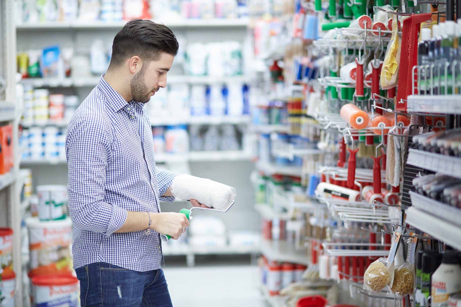 Man browsing shelves in a store aisle, holding a bottle and shopping basket