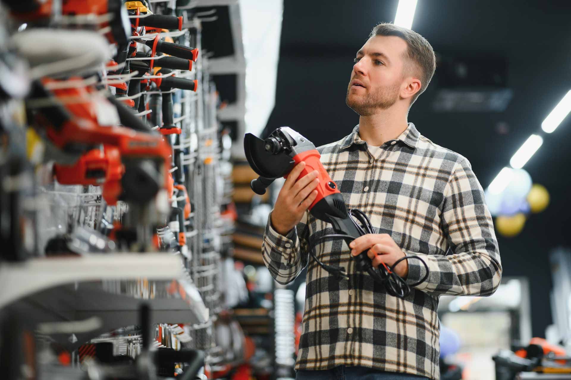 Technician inspecting power tools on store shelves, holding a red drill in a hardware store aisle