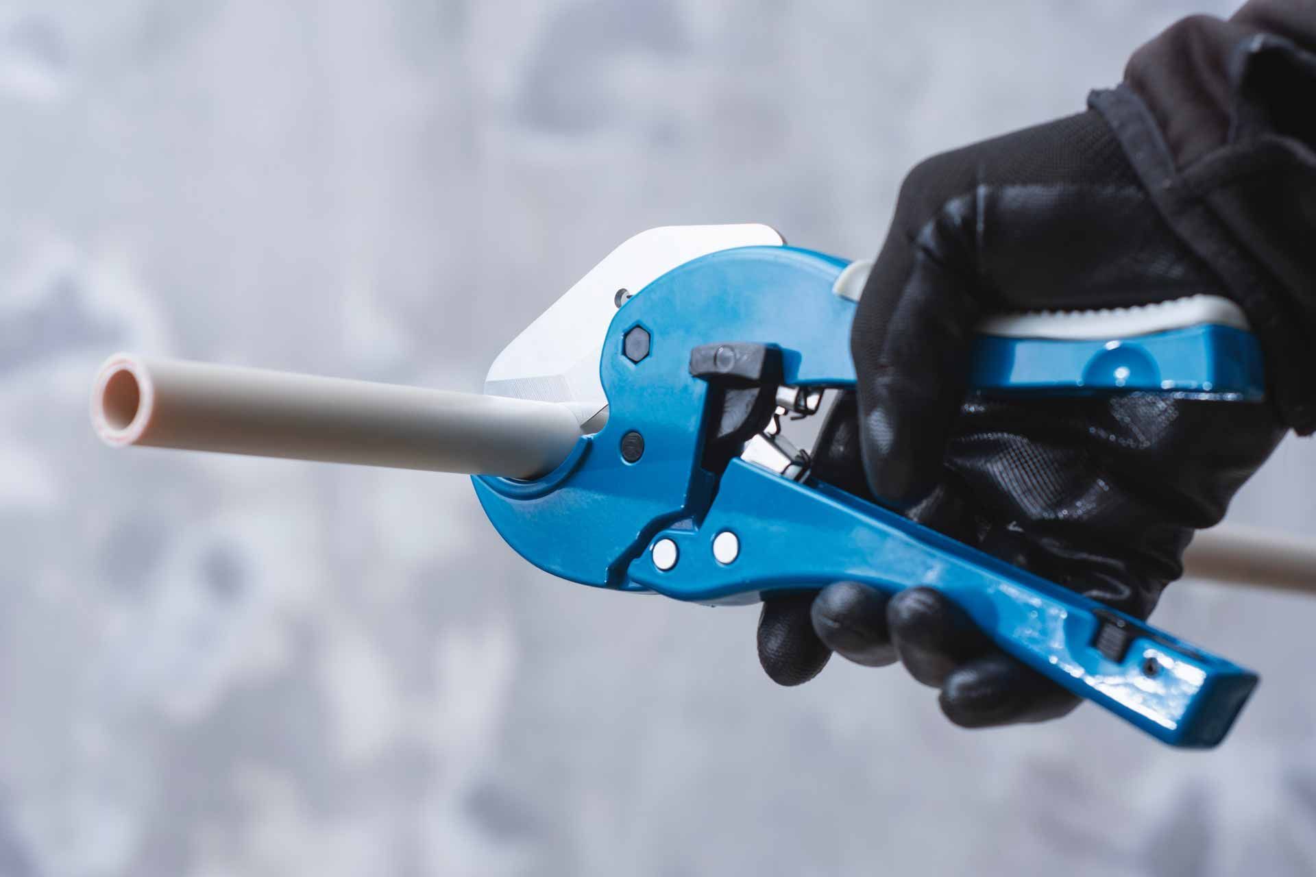 Gloved hand holding a blue pipe cutter around a gray PVC pipe against a blurred background