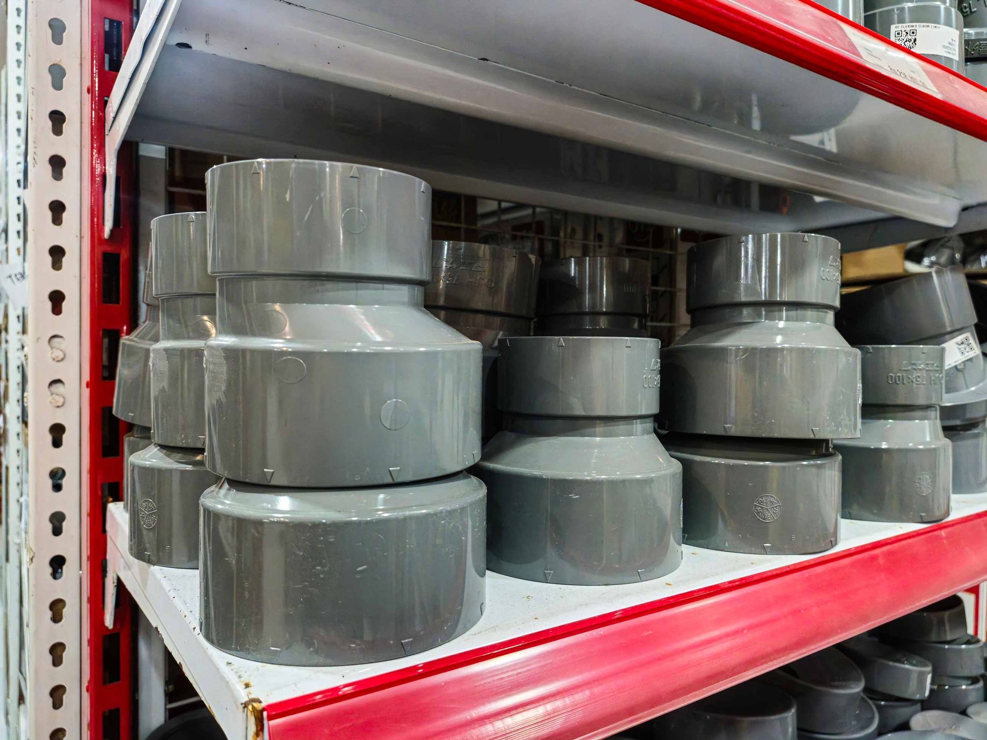 Stacked gray PVC pipe fittings on warehouse shelves with red supports