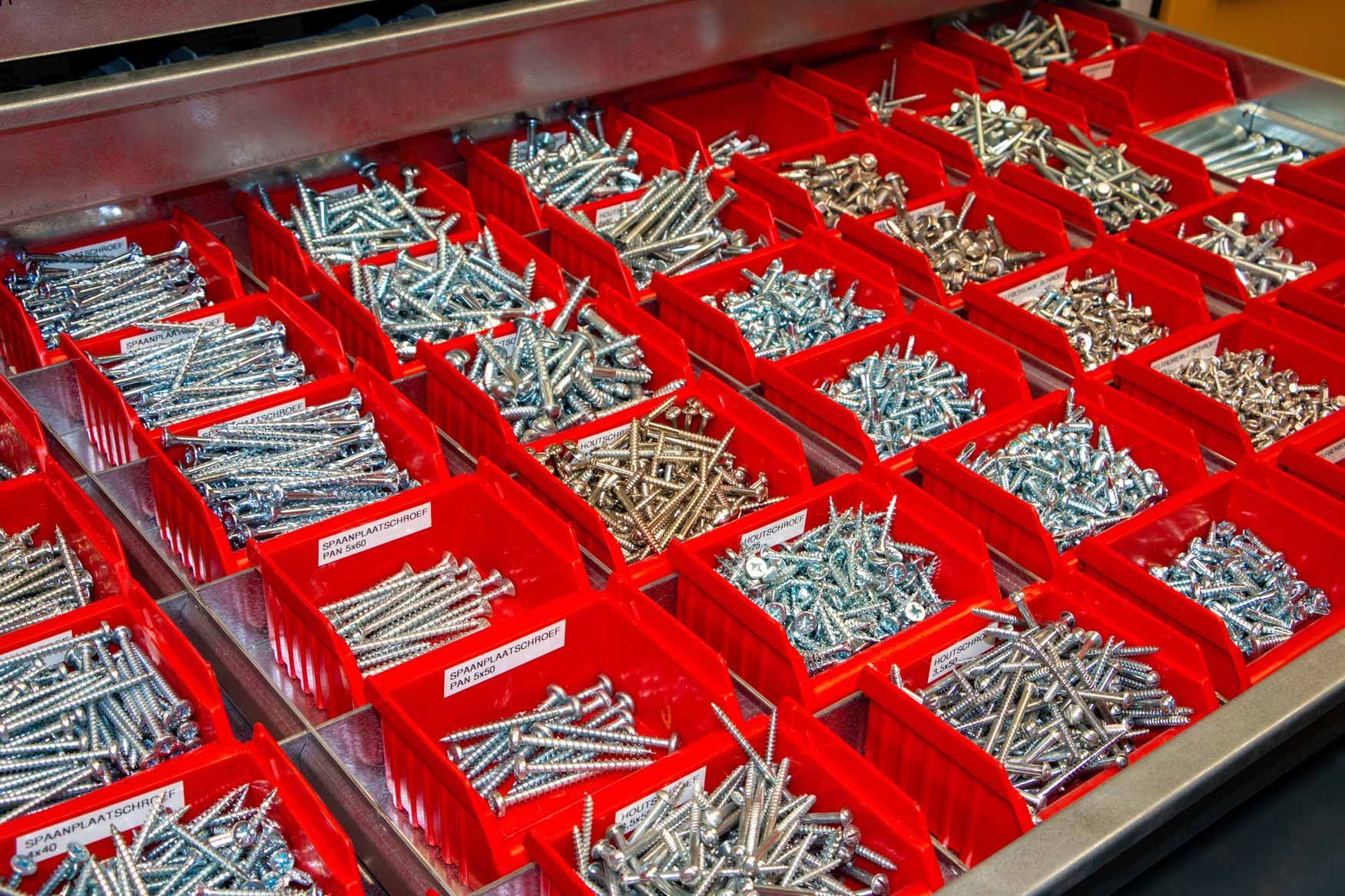 Red bins filled with assorted metal screws and fasteners in a hardware storage drawer