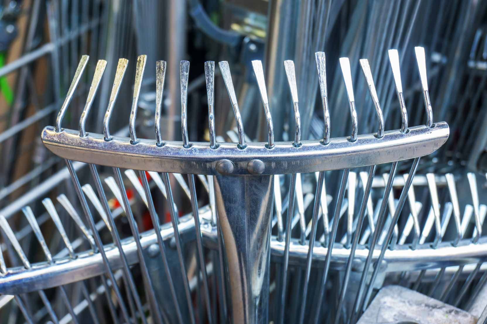 Metal garden rake head with tines stacked among other rakes in a store display