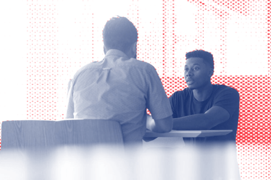 two men are sitting at a table having a conversation .