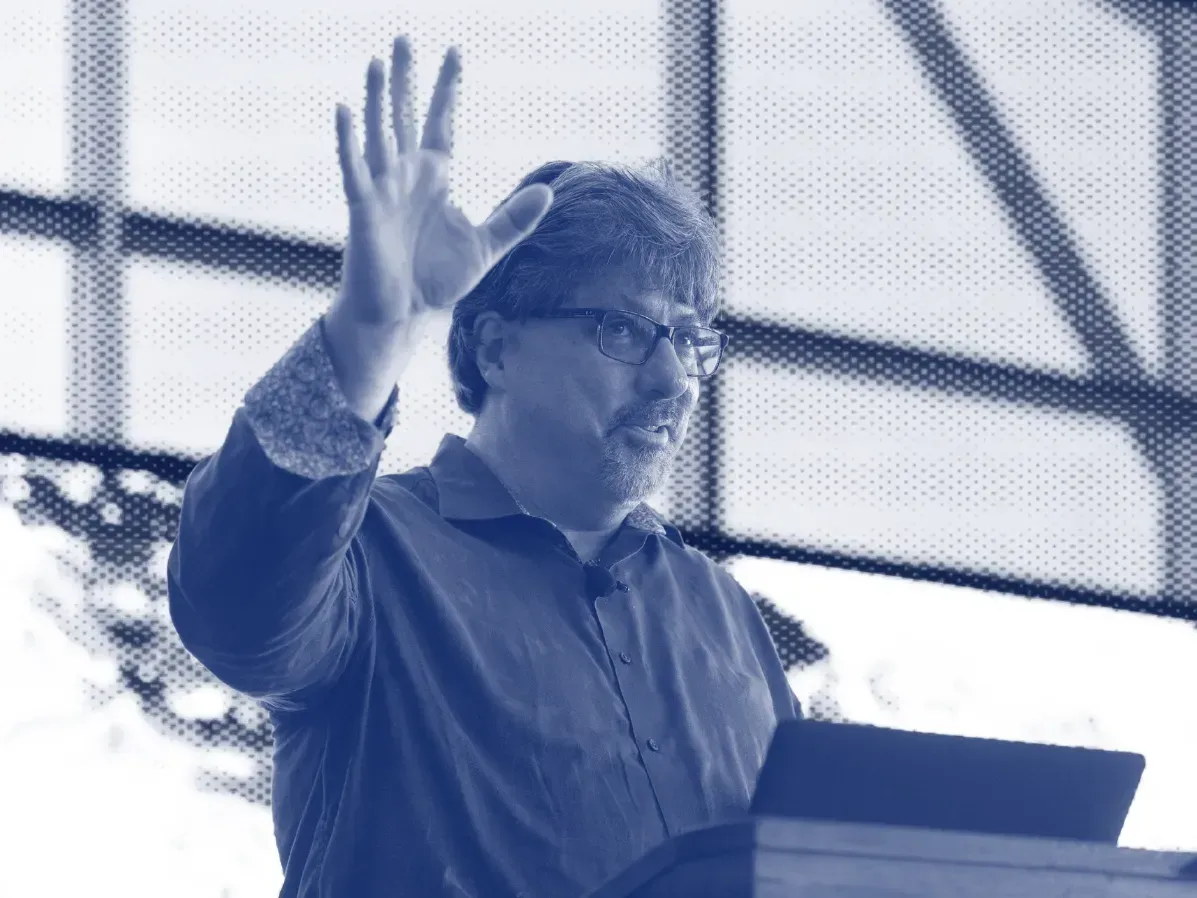 A man is standing at a podium giving a speech and waving his hand.