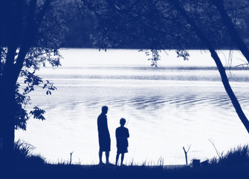 A man and a boy are standing on the shore of a lake