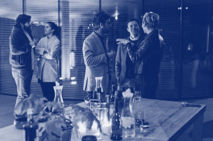 A group of people are standing around a table talking to each other.